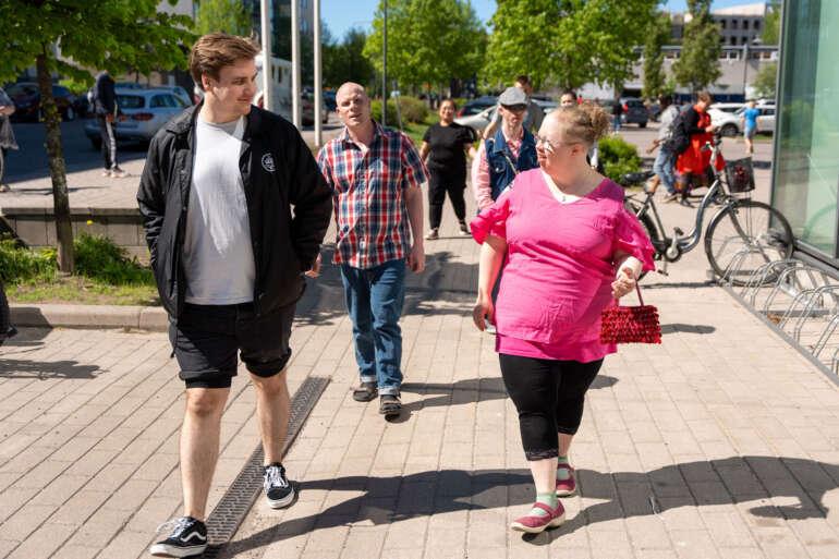 Vammaisten asumisyksikön asukkaita yhteisellä kävelyllä ulkona kirkkaassa säässä.